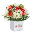 A playful spirit infuses this lively bouquet, arranged with the artistry and warmth characteristic of Spitalfields' independent florists. Ruffles of coral and vivid red carnations intermingle with snowy white daisies, their sun-bright green centers beaming like flecks of light across Commercial Street on a sunny day. Wisps of delicate baby's breath weave airily between the larger flowers, adding a gentle, cloud-soft touch and hinting at the creativity that flows through the East End. Deep, glossy green leaves provide structure and flair, sweeping around the base of the arrangement like an embrace. On the left, clusters of purple-blushed buds hint at the promise of new beginnings-a visual echo of the area's ongoing transformation and energy. All is gathered within a gleaming white square gift bag with silky ribbon handles, positioned against a purposefully plain background to spotlight the color and craftsmanship of each bloom. The bouquet radiates a sense of sincere happiness and modern elegance, perfect for commemorating joyful milestones, offering congratulations, or simply delivering a rush of cheer to homes and workplaces across Spitalfields. Each flower feels like a small celebration, thoughtfully curated for the lively rhythm of the local community.